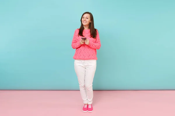 全长的妇女在针织毛衣 白色裤子短信短信在手机上隔离在明亮的粉红色蓝色柔和的墙壁背景下 在工作室 时尚生活方式的概念 模拟复制空间 — 图库照片