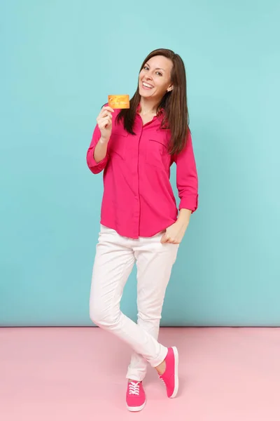 穿着玫瑰衬衫衬衫的年轻女子的全长肖像 白色裤子持有信用卡隔离在明亮的粉红色蓝色柔和墙背景工作室 时尚生活方式的概念 模拟复制空间 — 图库照片