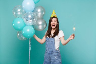 Sürpriz doğum günü şapkası ağzı açık, tutarak kadında tutun yanan maytap izole mavi turkuaz arka plan üzerinde renkli hava balonları ile kutluyor. Doğum günü tatil partisi, insanların duyguları kavramı