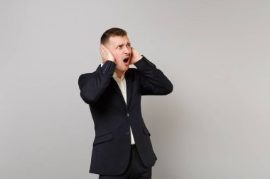 Bakılması, tahriş olmuş genç iş adamı el ile kulakları kapsayan klasik siyah elbiseli küfür Studio gri arka plan üzerinde izole. Başarı kariyer servet iş kavramı. Kopyalama alanı alay