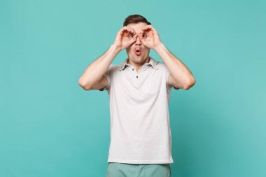 Genç adam gözleri, yakınındaki elele rahat kıyafetler gözlük veya izole mavi turkuaz duvar arka plan üzerinde dürbün taklit hayran. İnsanlar samimi duygular, yaşam kavramı. Kopyalama alanı alay