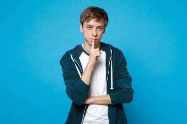 Rahat kıyafetler hush söyleyerek çekici genç adam portresi ile dudakları shhh jest mavi arka plan üzerinde izole parmağında sessiz ol. İnsanlar samimi duygular, yaşam kavramı. Kopyalama alanı alay