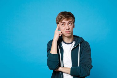 Yukarıya bakıp kafa mavi duvar arka plan üzerinde izole yakınındaki elini tutarak rahat kıyafetler dalgın genç adam portresi. İnsanlar samimi duygular yaşam tarzı kavramı. Kopyalama alanı alay. Reklam alanı