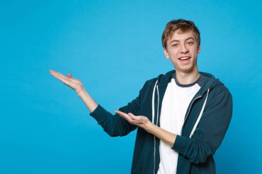 Rahat kıyafetler bir kenara Studio mavi arka plan üzerinde izole el işaret neşeli gülümseyen genç adam portresi. İnsanlar samimi duygular, yaşam kavramı. Kopyalama alanı alay. Reklam alanı
