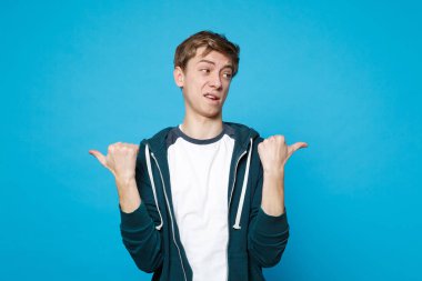 Ayakta, bir kenara Studio mavi duvar arka plan üzerinde izole başparmak işaret rahat kıyafetler şaşkın kendine güvenen genç adam portresi. İnsanlar samimi duygular, yaşam kavramı. Kopyalama alanı alay