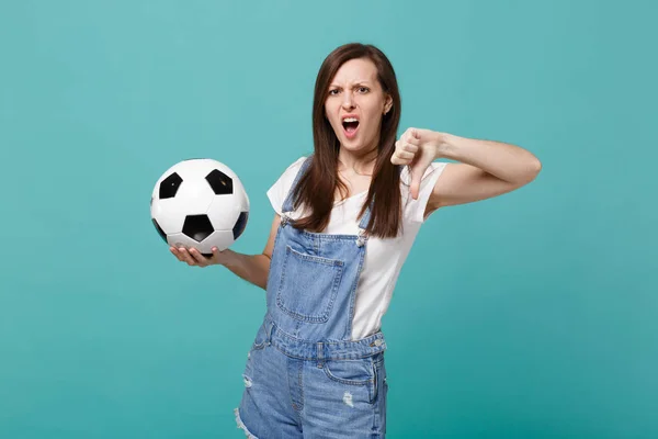 Irritated young woman football fan support favorite team with soccer ball showing thumb down isolated on blue turquoise background. People emotions, sport family leisure concept. Mock up copy space