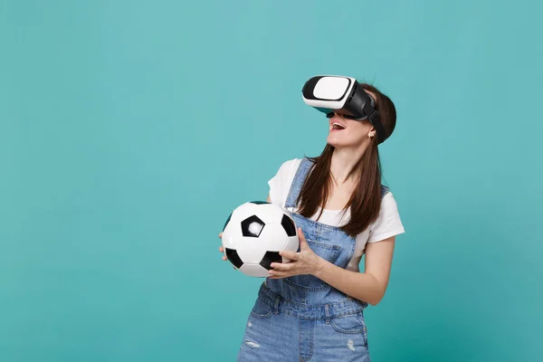 Excited young woman football fan looking in headset holding soccer ball playing isolated on blue turquoise wall background. People emotions, sport family leisure lifestyle concept. Mock up copy space