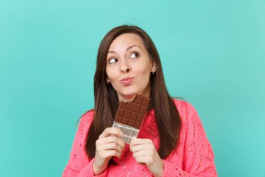 Örgü pembe kazaklı ararken, elinde tutan, mavi turkuaz duvar arka planda, stüdyo portre izole çikolata yemek rüya gibi genç kadın. İnsanlar yaşam tarzı kavramı. Kopyalama alanı alay