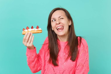 Komik ararken örme pembe kazaklı genç kadın, gösteren dil elinde mavi turkuaz duvar arka planda, stüdyo portre izole pasta kek tutun. İnsanlar yaşam tarzı kavramı. Kopyalama alanı alay
