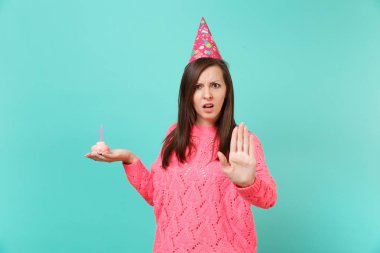 El üzerinde mavi arka plan izole mum ile pasta tutan söz konusu genç kadın örgü pembe kazaklı, palm, dur jestle gösterilen doğum günü şapkası. İnsanlar yaşam tarzı kavramı. Kopyalama alanı alay