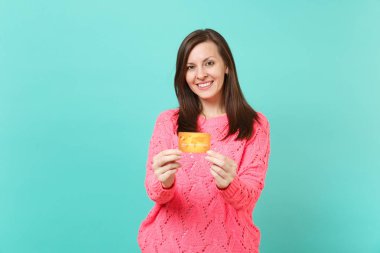 Örgü pembe kazak görünümlü kamera çekici genç kız gülümseyerek, elinde kredi kartı izole mavi turkuaz duvar arka plan stüdyo portre üzerinde tutun. İnsanlar yaşam tarzı kavramı. Kopyalama alanı alay