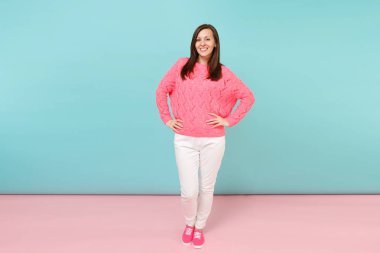 Tam uzunlukta örme gül kazaklı gülümseyen genç kadın portresi, beyaz parlak pembe mavi pastel duvar arka planda Studio izole poz pantolon. Moda yaşam tarzı kavramı. Kopyalama alanı alay