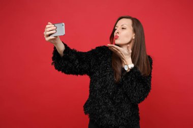 Pretty genç kız siyah kürk kazaklı selfie cep telefonu parlak kırmızı duvar arka plan üzerinde izole atış yapıyor gönderen hava öpücük üfleme. İnsanlar samimi duygular yaşam tarzı kavramı. Kopyalama alanı alay