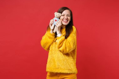 Sarı kürk kazaklı oldukça gülümseyen genç kadın portresi oyuncak ayı peluş oyuncak parlak kırmızı duvar arka planda Studio izole tutun. İnsanlar samimi duygular, yaşam kavramı. Kopyalama alanı alay