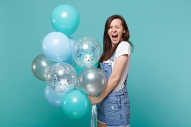 Komik genç kadın kutluyor, izole mavi turkuaz duvar arka plan üzerinde renkli hava balonları tutan denim giysiler içinde çığlık çılgın portresi. Doğum günü tatil partisi, insanların duyguları kavramı
