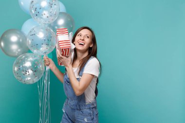 Hediye izole mavi turkuaz arka plan üzerinde renkli hava balonları ile şerit kutlama ile genç kız tutun Kırmızı şeritli mevcut kutusu gülüyor. Sevgililer günü, kadınlar günü, doğum günü, tatil kavramı