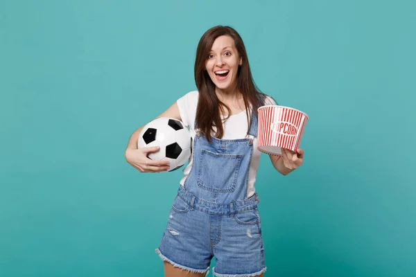 Excited young girl football fan watching match support favorite team with soccer ball, bucket of popcorn isolated on blue turquoise background. People emotions, sport family leisure lifestyle concept