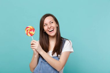 Denim giysileri ararken gülen çekici genç kadın portresi, holding renkli yuvarlak lolipop Studio turkuaz mavi zemin üzerine izole. İnsanlar yaşam tarzı kavramı. Kopyalama alanı alay