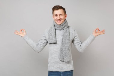 Gri süveterli genç adam gülümsüyor, eşarp el ele tutuşsun meditasyon izole üzerinde gri arka plan rahatlatıcı yoga hareketle. Sağlıklı yaşam tarzı insanların samimi duygular soğuk sezon kavramı. Kopyalama alanı alay