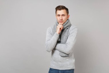 Kendine güvenen genç adam gri süveterli Studio gri arka plan üzerinde izole çene üzerinde yukarı koymak el pervane eşarp. Sağlıklı moda yaşam tarzı, insanlar samimi duygular, soğuk sezon kavramı. Kopyalama alanı alay