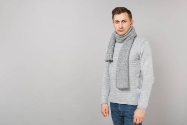 Genç adam gri süveterli gülümseyen portresi, Studio gri duvar arka plan üzerinde duran eşarp izole. Sağlıklı moda yaşam tarzı, insanlar samimi duygular, soğuk sezon kavramı. Kopyalama alanı alay