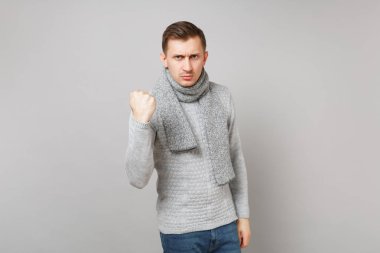 Sıkı genç adam gri süveterli gösterilen, eşarp Studio gri duvar arka plan üzerinde izole yumruk kasılıyor. Sağlıklı moda yaşam tarzı, insanlar samimi duygular, soğuk sezon kavramı. Kopyalama alanı alay