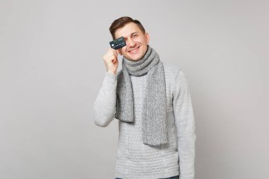 Gri süveterli kredi banka kartı ile göz kapsayan eşarp neşeli genç adam gri arka plan üzerinde izole. Sağlıklı moda yaşam tarzı, insanlar samimi duygular, soğuk sezon kavramı. Kopyalama alanı alay