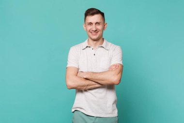 Genç adam ayakta ve el ele tutuşarak katlanmış rahat kıyafetler içinde gülümseyen bir portre Studio mavi turkuaz duvar arka plan üzerinde izole. İnsanlar samimi duygular, yaşam kavramı. Kopyalama alanı alay
