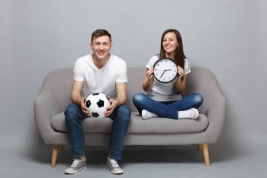 Eğlenceli çift kadın adam futbol taraftarları beyaz t-shirt gri duvar arka plan üzerinde izole yuvarlak saat tutan futbol topu ile destek favori takım tezahürat. İnsanlar spor aile eğlence yaşam tarzı kavramı