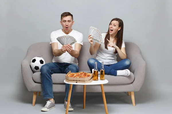 Amazed couple woman man football fans cheer up support favorite team holding fan of money in dollar banknotes, cash money isolated on grey background. People sport family leisure lifestyle concept