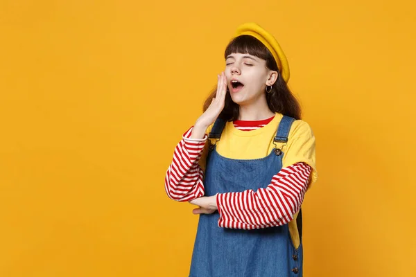 眠そうな少女でティーンエイ ジャーの肖像フランス ベレー帽 スタジオの背景が黄色に分離されたデニム サンドレスあくび 維持目を閉じています の心から感情 ライフ スタイルのコンセプト コピー — ストック写真