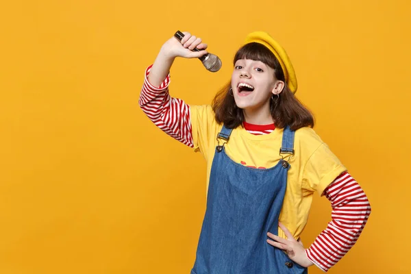 有趣的女孩少年的肖像在法国贝雷帽和牛仔太阳礼服唱歌在麦克风孤立的黄色墙壁背景在工作室 人们真诚的情感 生活方式的理念 模拟复制空间 — 图库照片