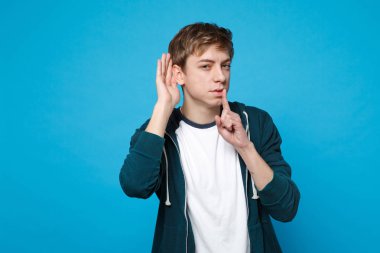 Meraklı genç adam söyleyerek hush dudaklar shhh hareketi, parmakta ile sessiz ol kulak misafiri ve izole üzerinde mavi arka plan stüdyo işitme. İnsanlar samimi duygular, yaşam kavramı. Kopyalama alanı alay