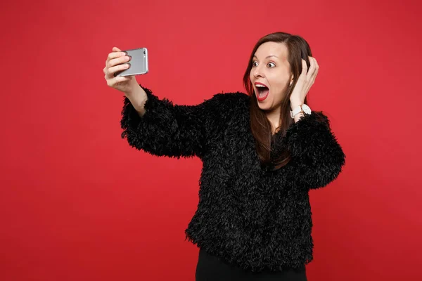 Excited young woman in black fur sweater clinging to head, doing