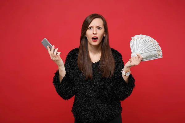 Perplex jonge vrouw in zwarte vacht trui houden van mobiele telefoon, — Stockfoto