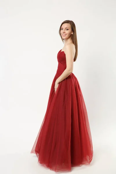 Full length photo fashion model woman wearing elegant evening dress red gown posing isolated on white wall background studio portrait. Brunette long hair girl. Mock up copy space. Side profile view. — Stock Photo, Image