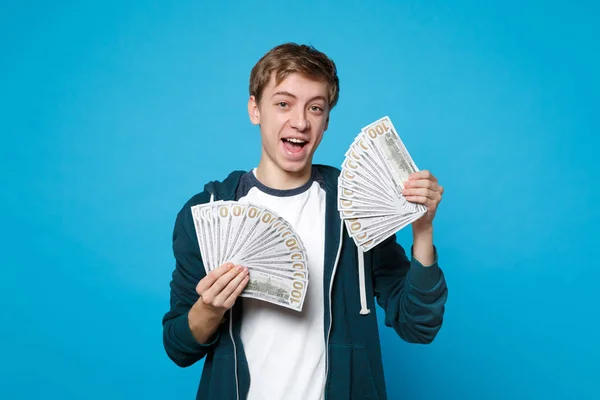 Χαρούμενα αστεία νεαρός άνδρας στο casual ρούχα κρατώντας ανεμιστήρα του χρήματος — Φωτογραφία Αρχείου