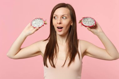 Hayran genç kadın bir kenara stüdyo pembe pastel duvar arka planda izole taze olgun pitahaya ejderha meyve halfs tutarak bakıyor. İnsanlar canlı yaşam tarzı tatil konsepti rahatlayın. Kopya alanı mock.