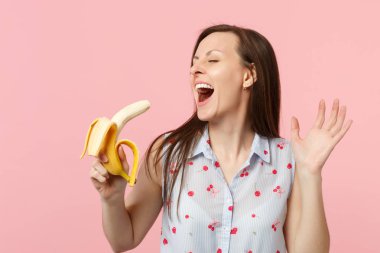 Yaz giysileri gözleri kapalı tutarak gülmek genç kadın, pembe pastel duvar arka planda izole taze olgun muz meyve tutarak. İnsanlar canlı yaşam tarzı, tatil konsepti rahatlayın. Kopya alanı mock.