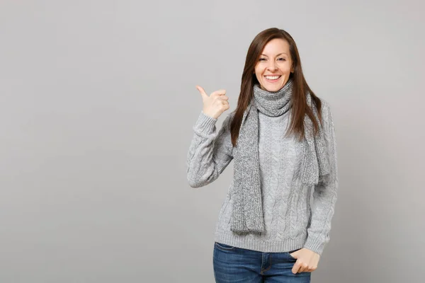 Mujer joven sonriente en suéter gris, bufanda señalando el pulgar a un lado —  Fotos de Stock