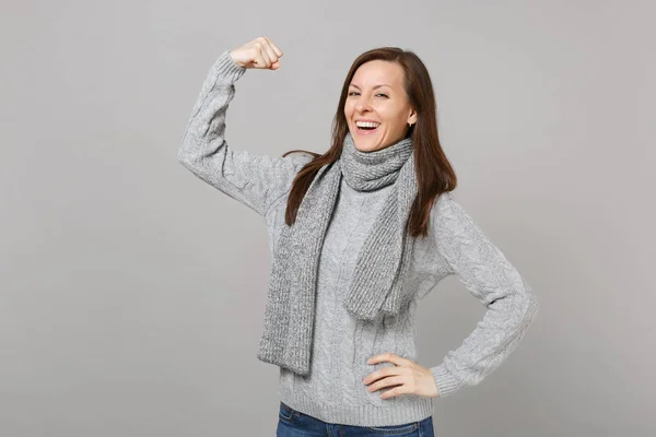 Mujer joven sonriente en suéter gris bufanda que muestra músculos del bíceps —  Fotos de Stock