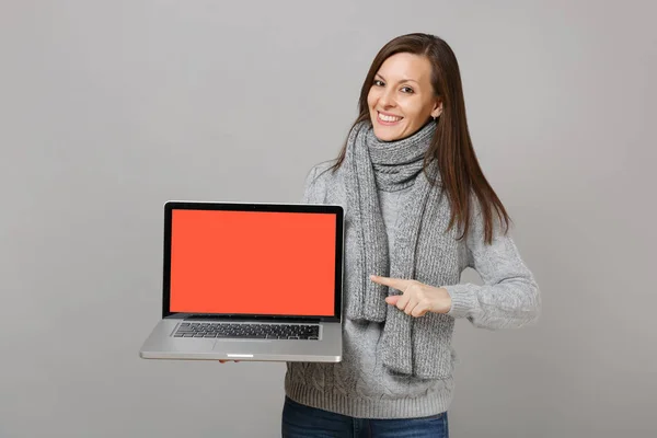 Χαμογελαστή γυναίκα με γκρι πουλόβερ, κασκόλ σημείο δείκτη δάχτυλο στο Lapto — Φωτογραφία Αρχείου