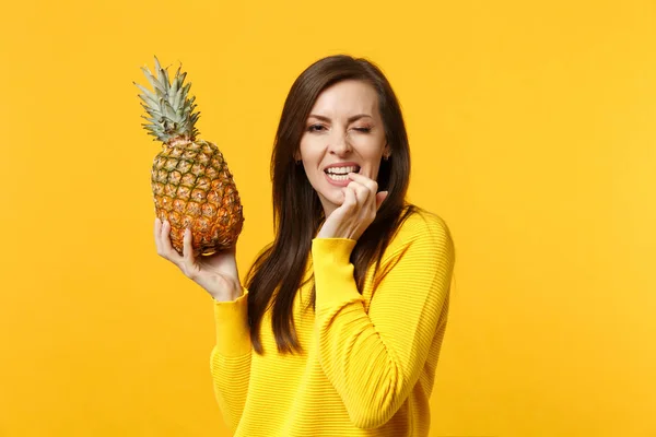 Mujer joven parpadeante con ropa casual royendo uñas, sostenga en las manos fruta fresca de piña madura aislada sobre fondo amarillo anaranjado. Gente estilo de vida vívido, relajarse concepto de vacaciones. Simular espacio de copia . —  Fotos de Stock