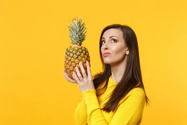 Mujer joven pensativa con ropa casual mirando hacia arriba, sosteniendo fruta fresca de piña madura aislada sobre fondo amarillo anaranjado en el estudio. Gente estilo de vida vívido, relajarse concepto de vacaciones. Simular espacio de copia . —  Fotos de Stock