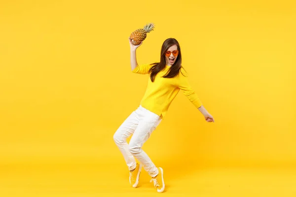 Giovane donna allegra in bicchieri di cuore che balla, tenendo frutta fresca matura ananas isolato su sfondo giallo parete arancione in studio. Persone vivido stile di vita, rilassarsi concetto di vacanza. Falsificare spazio di copia . — Foto Stock