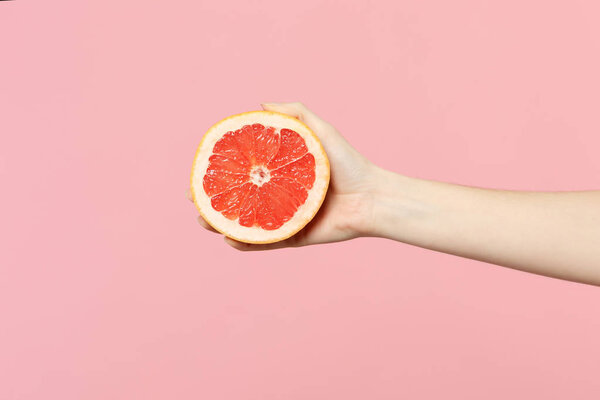 Close up cropped photo of female hold in hand fresh ripe half grapefruit fruit isolated on pink pastel wall background. Copy space advertising mock up. People vivid lifestyle, relax vacation concept.