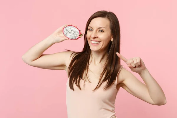 Smiling young woman pointing index finger on half of fresh ripe pitahaya, dragon fruit isolated on pink pastel background in studio. People vivid lifestyle relax vacation concept. Mock up copy space.