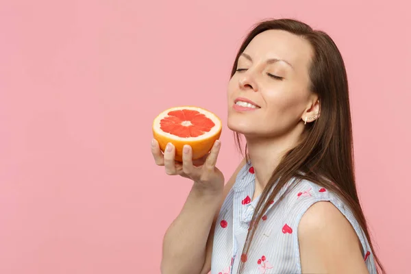 Relaxed young woman in summer clothes keeping eyes closed, holding half of fresh ripe grapefruit isolated on pink pastel background. People vivid lifestyle relax vacation concept. Mock up copy space.