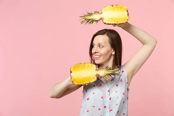 Hermosa joven vestida con ropa de verano mirando a un lado sosteniendo mitades de fruta fresca de piña madura aislada sobre fondo pastel rosado. La gente estilo de vida vívido relajar concepto de vacaciones. Simular espacio de copia . —  Fotos de Stock