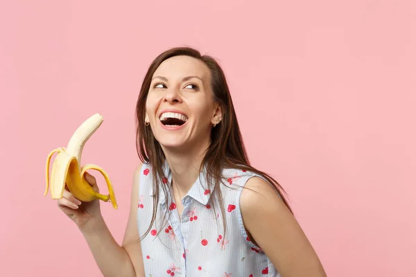 Joven riéndose con ropa de verano mirando hacia arriba sosteniendo fruta fresca de plátano madura aislada sobre fondo de pared de pastel rosa en el estudio. La gente estilo de vida vívido relajar concepto de vacaciones. Simular espacio de copia . —  Fotos de Stock